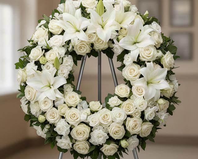 Corona funeraria de rosas y lirios blancos sobre soporte metálico